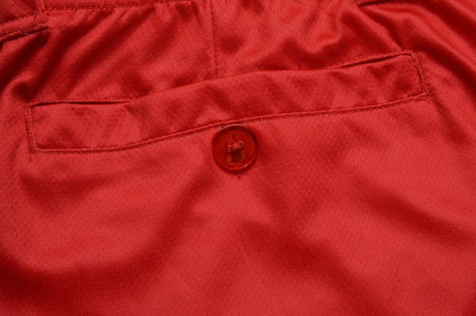 A close-up of red fabric with a button and a pocket detail. The material has a smooth texture.