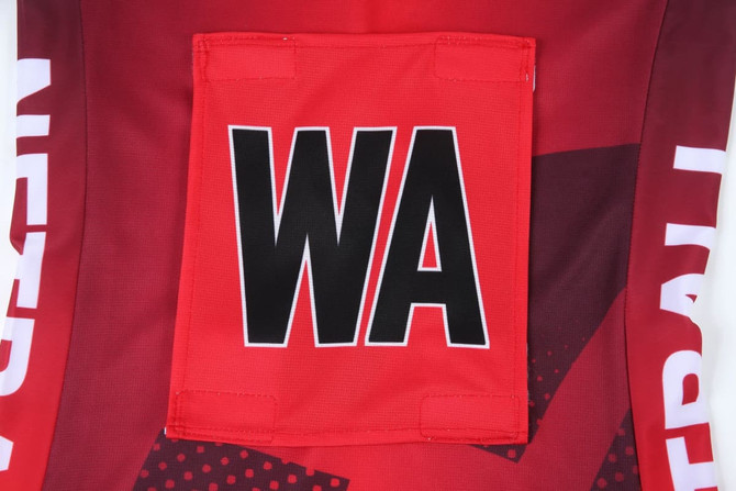 A red netball dress featuring a large black "WA" patch and a geometric design on the fabric.