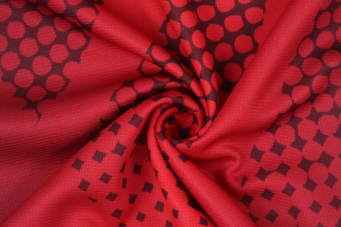 A red fabric with a textured pattern of circles and squares, featuring a smooth, swirling design.