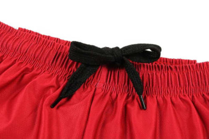 A close-up of a red soccer uniform showing the waistband and black drawstring. It features a logo.