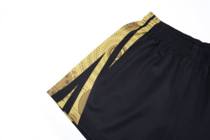 Aboriginal AFL shorts featuring a distinctive black and gold design with abstract patterns and a logo.