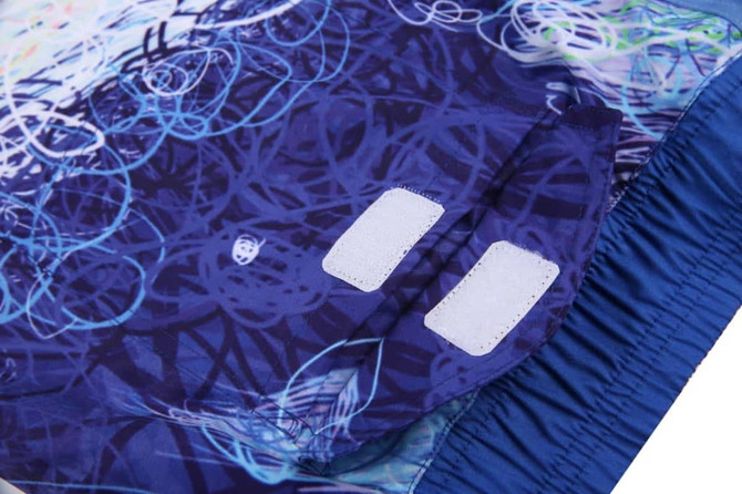 A pair of board shorts featuring a swirling pattern in blue, with a solid blue waistband and two Velcro patches.