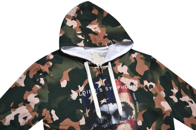 A 100% cotton hoodie in a camouflage pattern, featuring a large graphic print and a logo on the front.