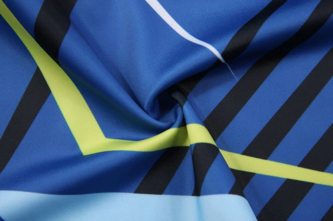 A close-up of a blue fabric featuring bold geometric patterns in green and black, with a smooth texture.