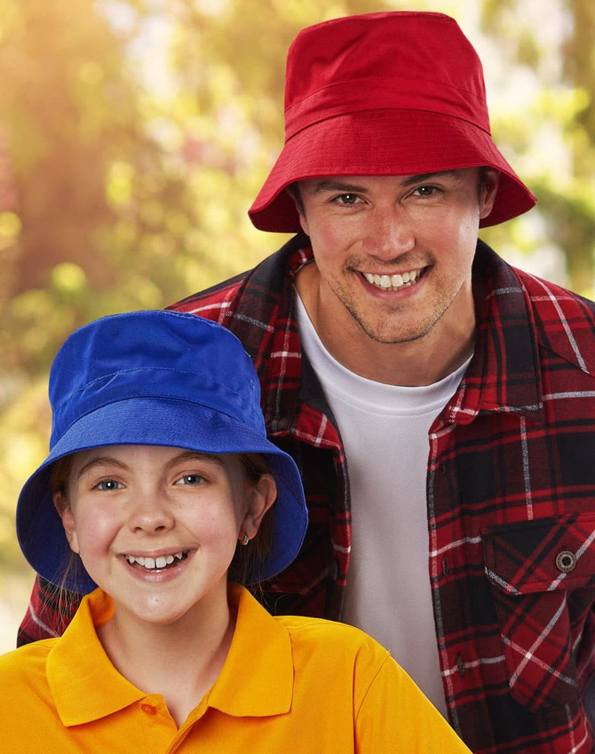 A red bucket hat and a blue bucket hat are worn by a smiling man and girl outdoors. Both hats feature a toggle.