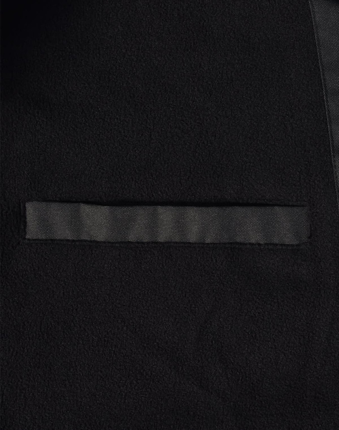 A close-up of a black long line stadium jacket featuring a sleek design and a pocket. The jacket has a branding logo.