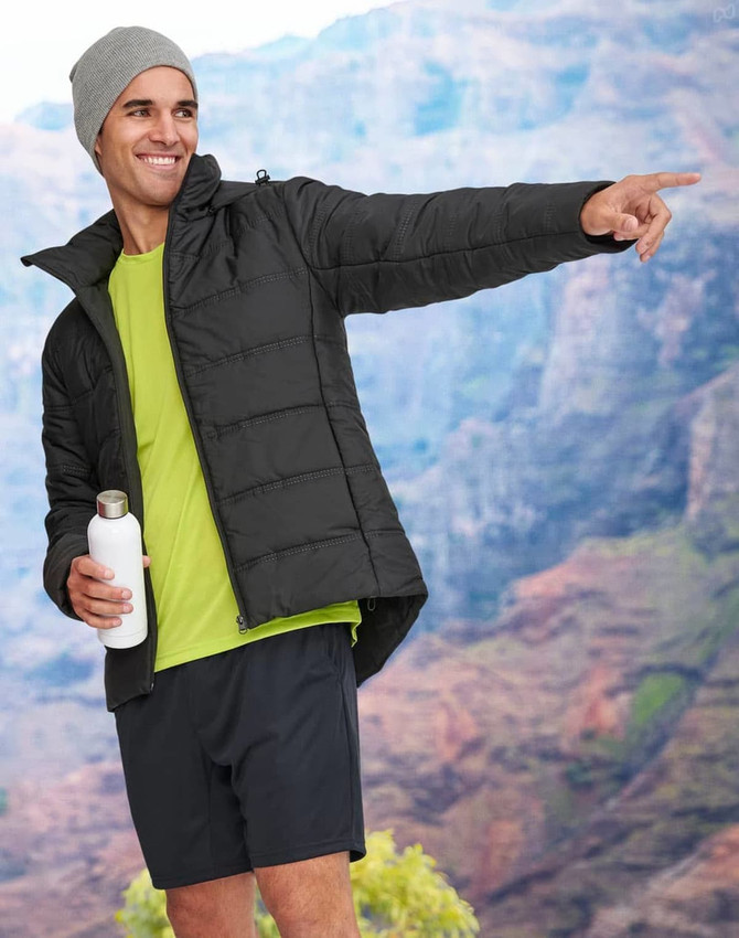 A model in a black sustainable parka jacket with a grey beanie, holding a drink bottle, set against a mountainous backdrop.