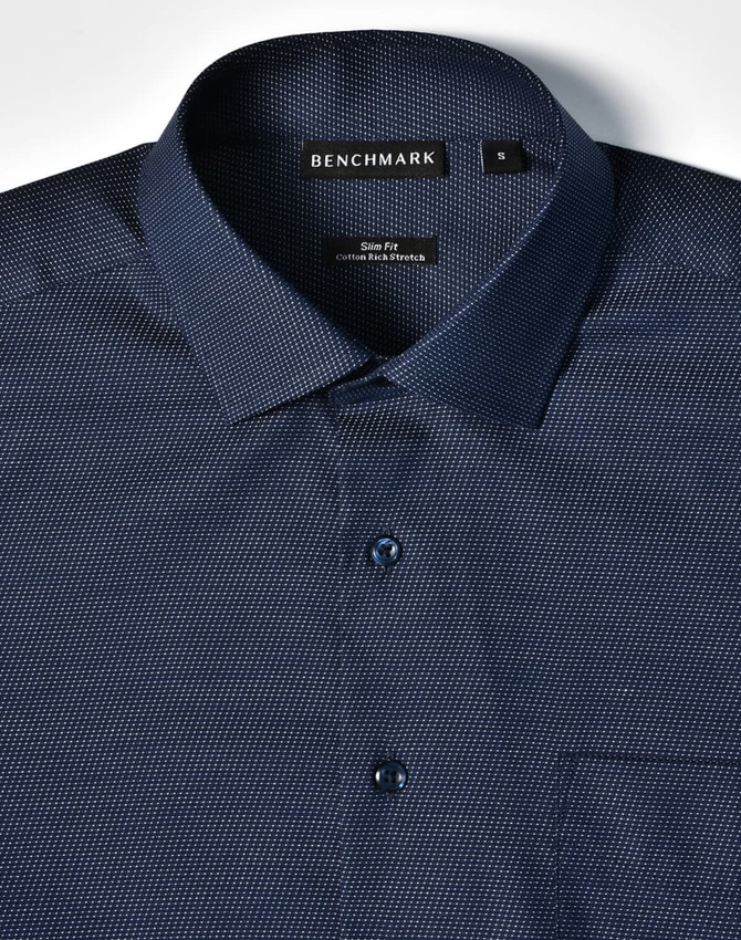 A navy blue button-up shirt featuring a pin dot pattern, with a single chest pocket and a branded label.