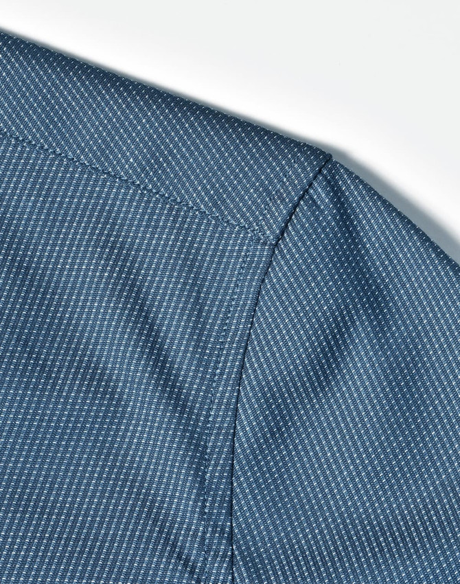 A close-up of a blue pin dot pattern on a 3/4 sleeve shirt, featuring a button-up design.
