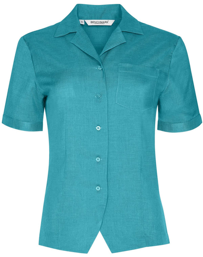 A short sleeve overblouse in teal with a collar, buttons, and a chest pocket. It features a logo on the label.