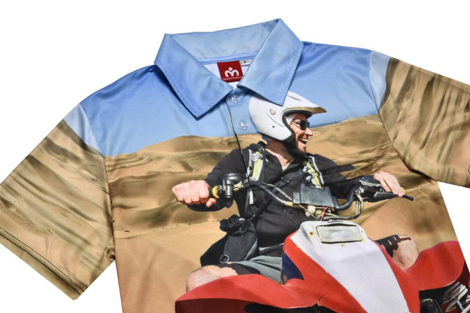 A polo shirt featuring a vibrant desert scene with shades of blue and beige, and a logo on the collar.
