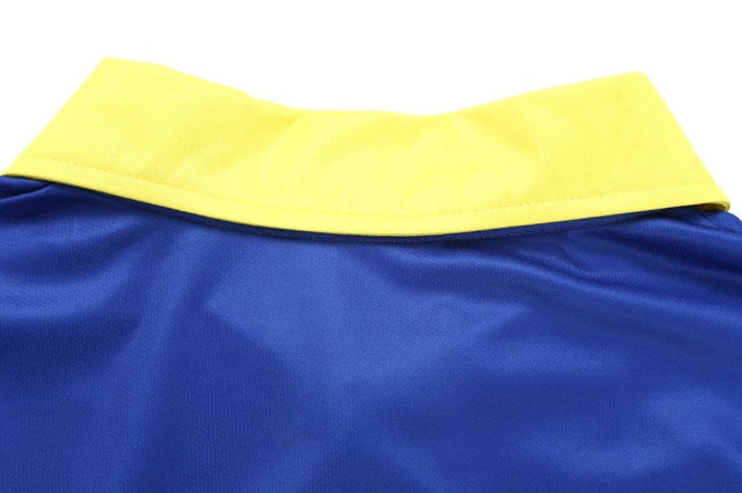 A blue cricket polo shirt with a yellow collar, featuring stitching details and a smooth fabric texture.