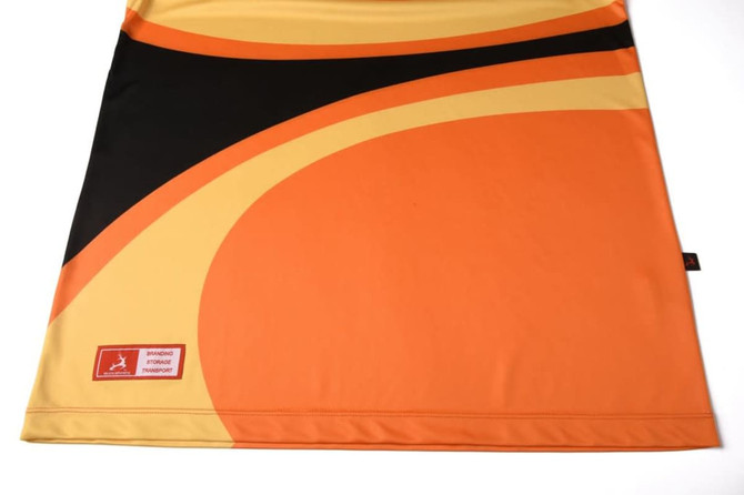 A customised polo featuring vibrant orange, black, and yellow patterns with a logo on the bottom corner.