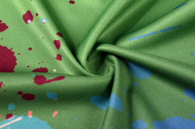 A green fabric featuring a splash design with red and blue accents, suitable for a running singlet.