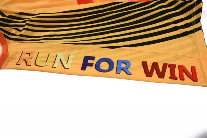 A vibrant orange and yellow singlet with bold lettering and a striped design. The singlet has a logo on it.