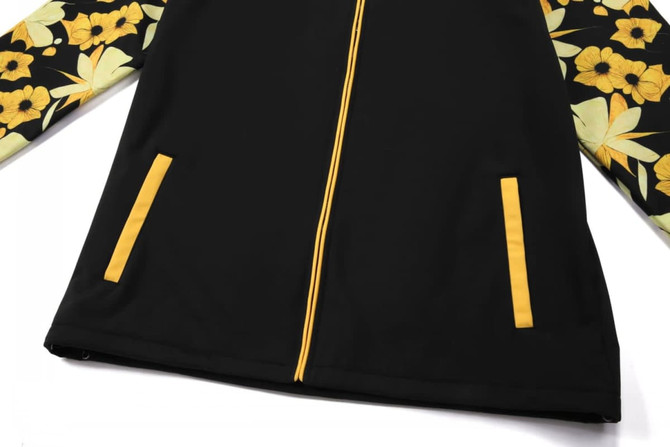 A black jacket with floral patterned sleeves in shades of yellow and green, featuring two front pockets and a zipped closure.