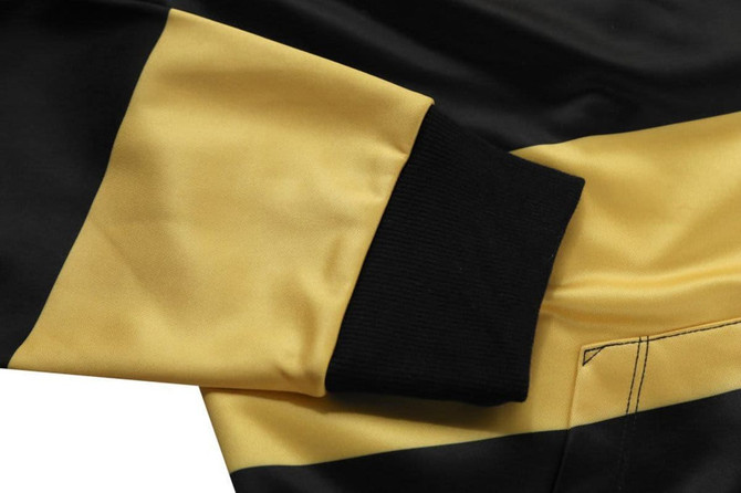 A close-up of a black and yellow kangaroo hoodie featuring a ribbed black cuff. The hoodie has a smooth fabric texture.