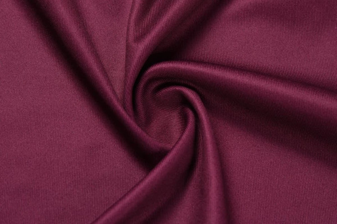A close-up of burgundy fabric, displaying a smooth and stretchy texture with a slight sheen.