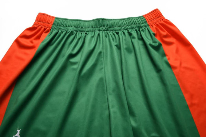 Green and orange junior soccer shorts with an elastic waistband and a logo on one side.