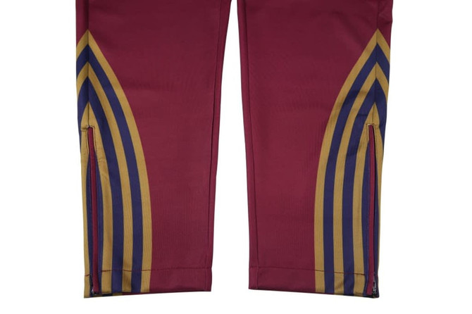 Zipper bottom training pants in maroon, featuring decorative stripes in gold, blue, and red. Includes a small logo.
