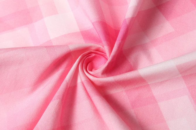 A close-up of soft, pink checkered fabric with a smooth texture. The material showcases a spiral pattern.