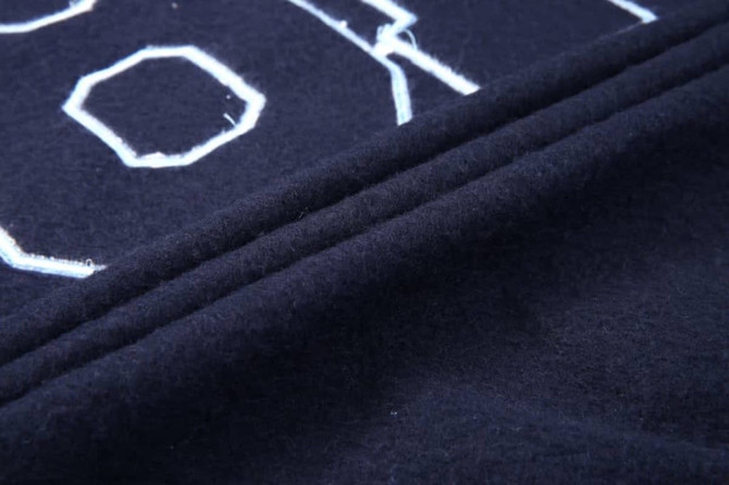 A close-up of a navy collegiate jacket fabric featuring textured lettering and stitched details.