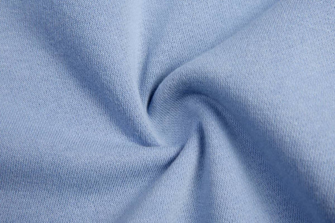 A fabric swirl in light blue, showcasing soft, dyed cotton material. Features a subtle, textured weave.
