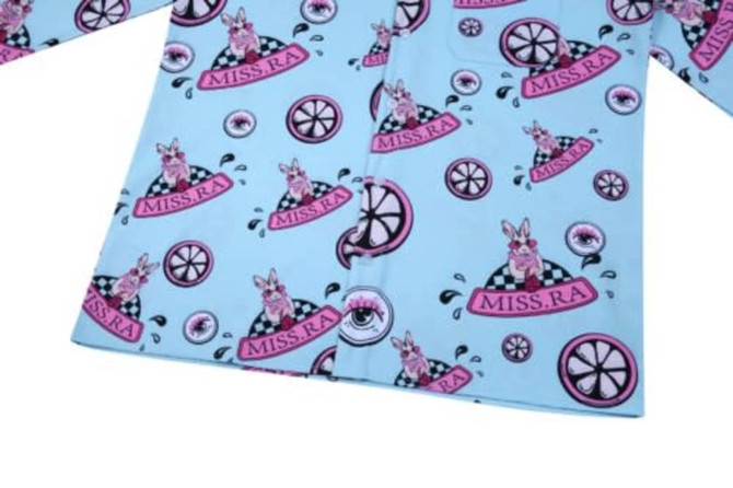 A light blue shirt featuring a playful pattern with pink bunnies, wheels, and various circular designs.