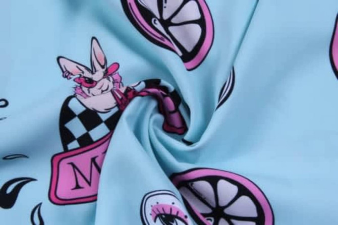 A fabric with a light blue background featuring playful illustrations of a bunny, lemons, and various patterns in pink and black.