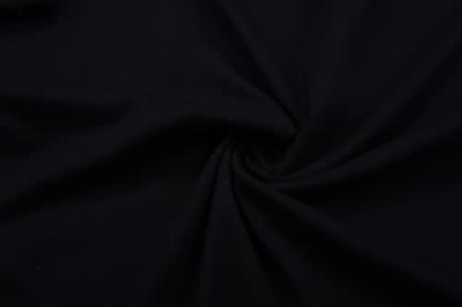 A black cotton T-shirt fabric twisted in a spiral pattern. The material appears smooth and flexible.