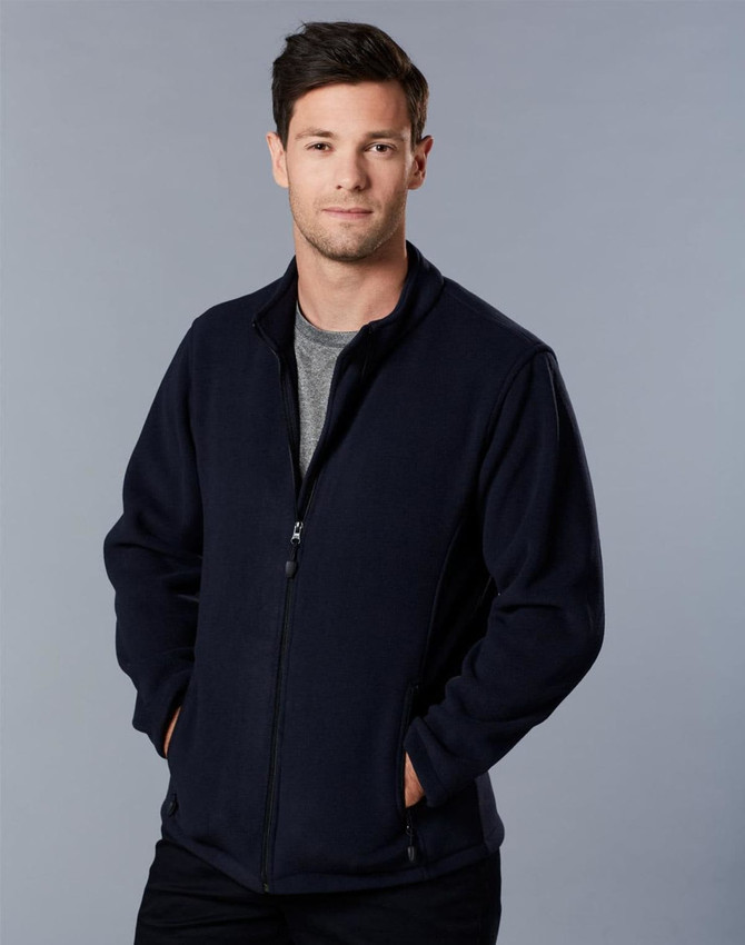 A man in a navy polar fleece jacket with a full zip, standing with hands in pockets against a grey background.