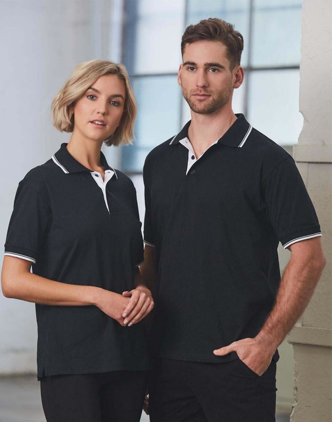 A unisex black polo shirt featuring white detailing, modelled by a man and woman in an indoor setting.