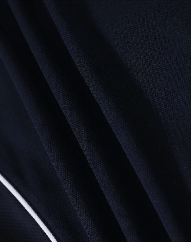 Close-up of a navy blue polo shirt fabric with a textured pattern and white detailing. The shirt features a logo.
