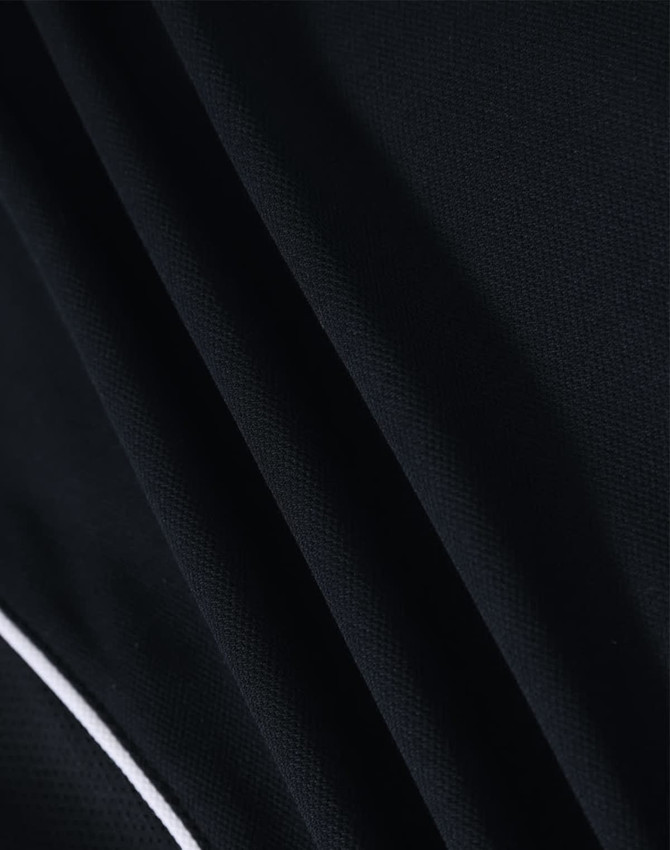 A close-up of a black fabric featuring textured folds, part of a Ladies S/S Sport Polo shirt with a branding logo.