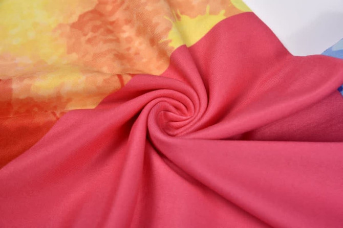 A close-up of fabric featuring vibrant orange, pink, and blue colours, displaying a soft, textured surface.