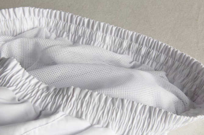 A close-up of white tracksuit pants featuring a mesh interior and elastic waistband, showcasing the fabric texture.
