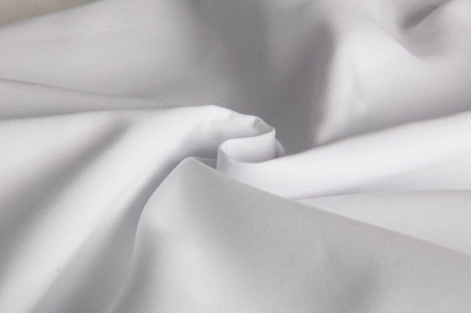 A close-up of white fabric, showcasing its smooth texture and folds. The image features a subtle sheen.