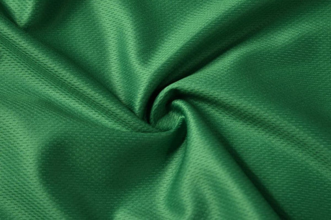 A textured green fabric with a smooth finish, featuring a slight sheen and a twisted appearance.