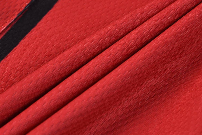 Red tracksuit bottoms made from textured fabric, featuring folds and a black accent. Includes a logo.