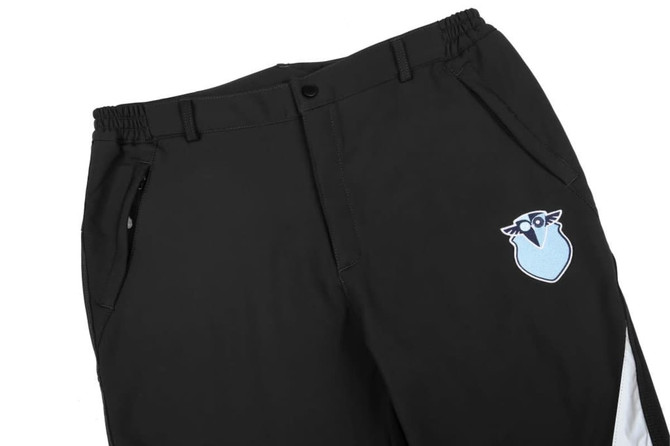 Softshell pants in black with a blue and white logo on the front, featuring an elastic waistband and zippered pockets.