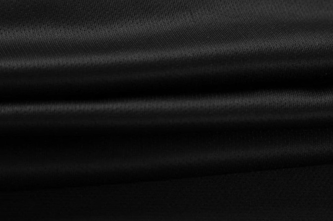 A close-up of smooth, black fabric featuring soft folds and a subtle sheen.