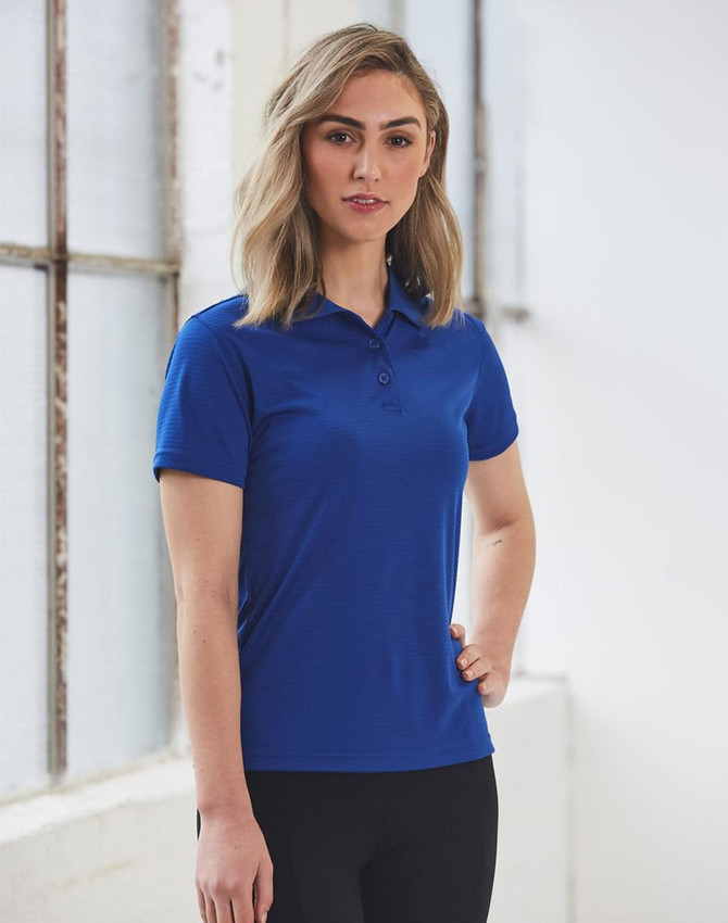 A woman stands wearing a ladies' textured polo shirt in blue, featuring a collar and a logo.
