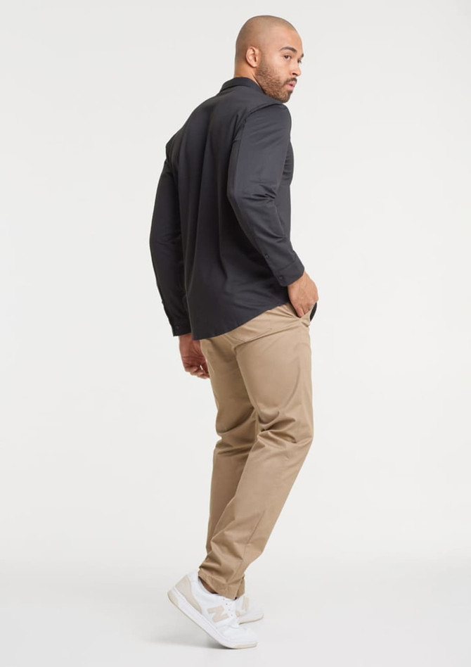 A man wearing a black long sleeve shirt and beige pants, standing with his back towards the camera.