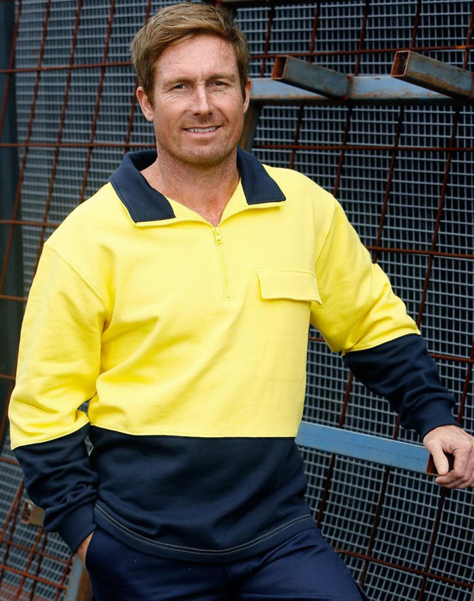 A man wearing a hi-vis two-tone yellow and navy cotton fleecy sweatshirt with a zip and pocket, posed against a metal backdrop.