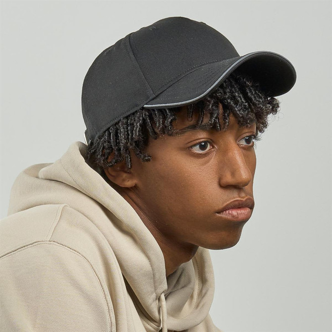 A black cap with a smooth finish and a logo, worn by a person with curly hair and wearing a hoodie.