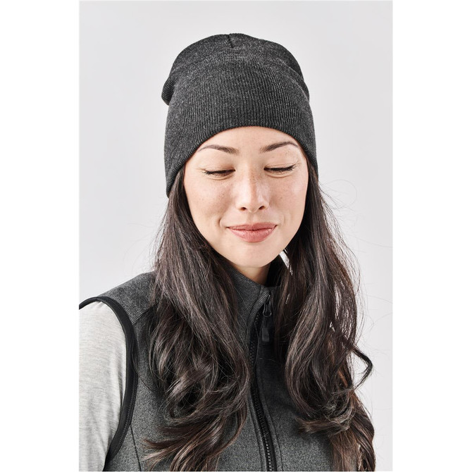 A woman wearing a dark grey knit beanie, showcasing a snug fit and a textured pattern. The beanie has a logo.