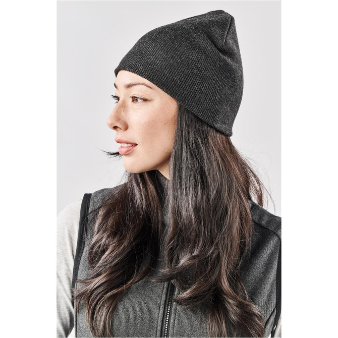 A dark grey knit beanie worn by a woman with long hair, featuring a simple design and a fitted shape.