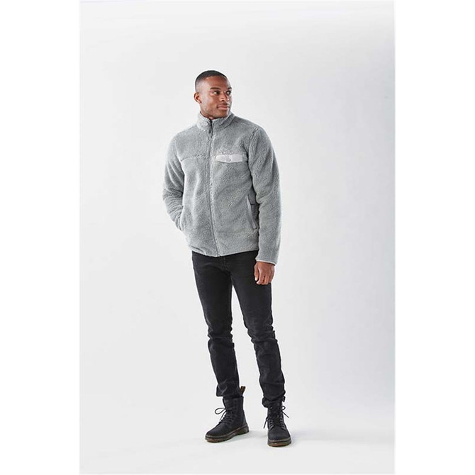 A grey Sherpa fleece jacket with a zip and a front pocket, worn by a man styled with black trousers and boots.