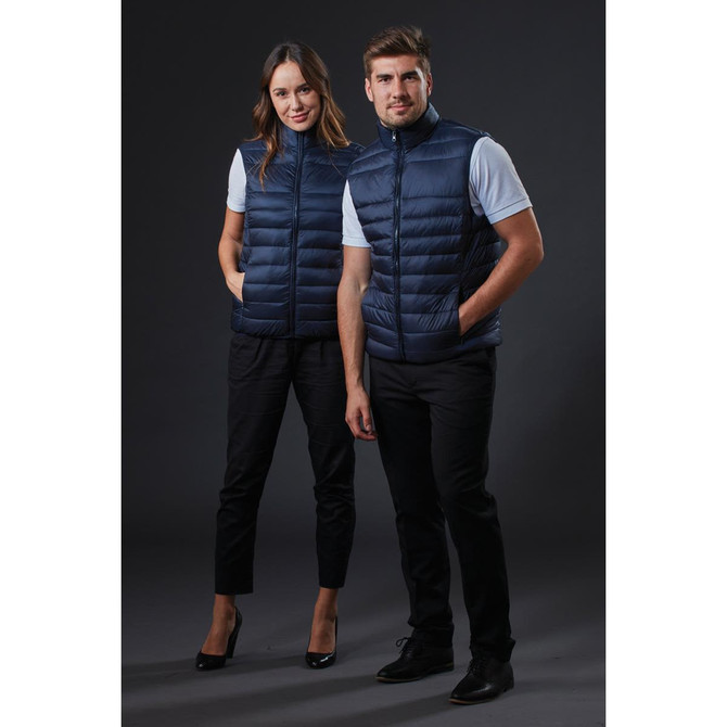 Two models wearing navy blue puffer vests, standing side by side against a dark background. The vests have a zip closure and a sleek design.