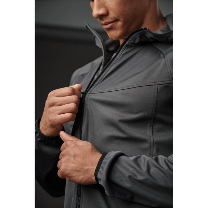 A man zips up a dark grey softshell jacket, showcasing its streamlined design and fit. The jacket has a hood and cuff detailing.